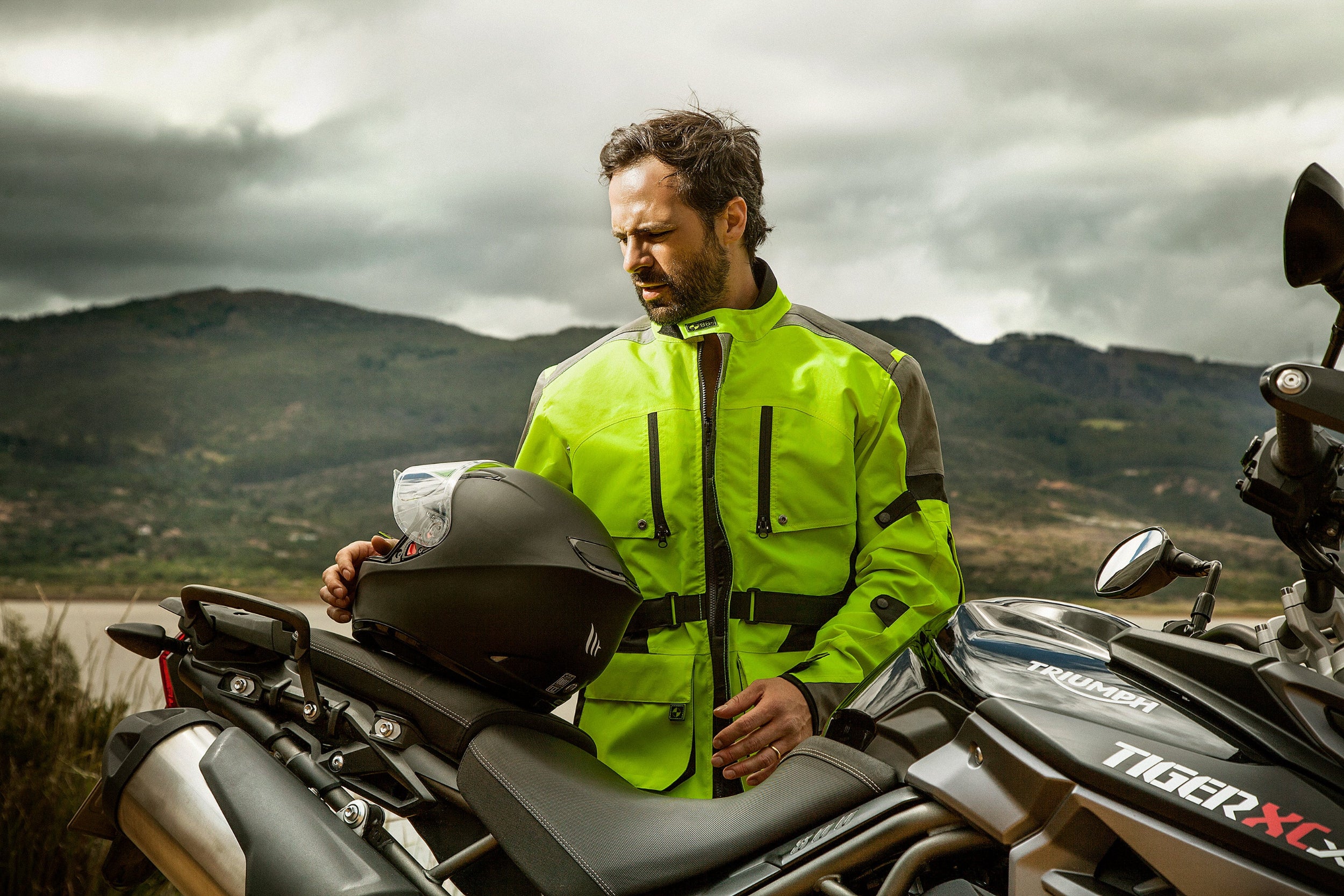 Motorista conduciendo una moto tipo trail/adventure en carretera, protegido con la chaqueta con airbag integrada gris y amarillo neon