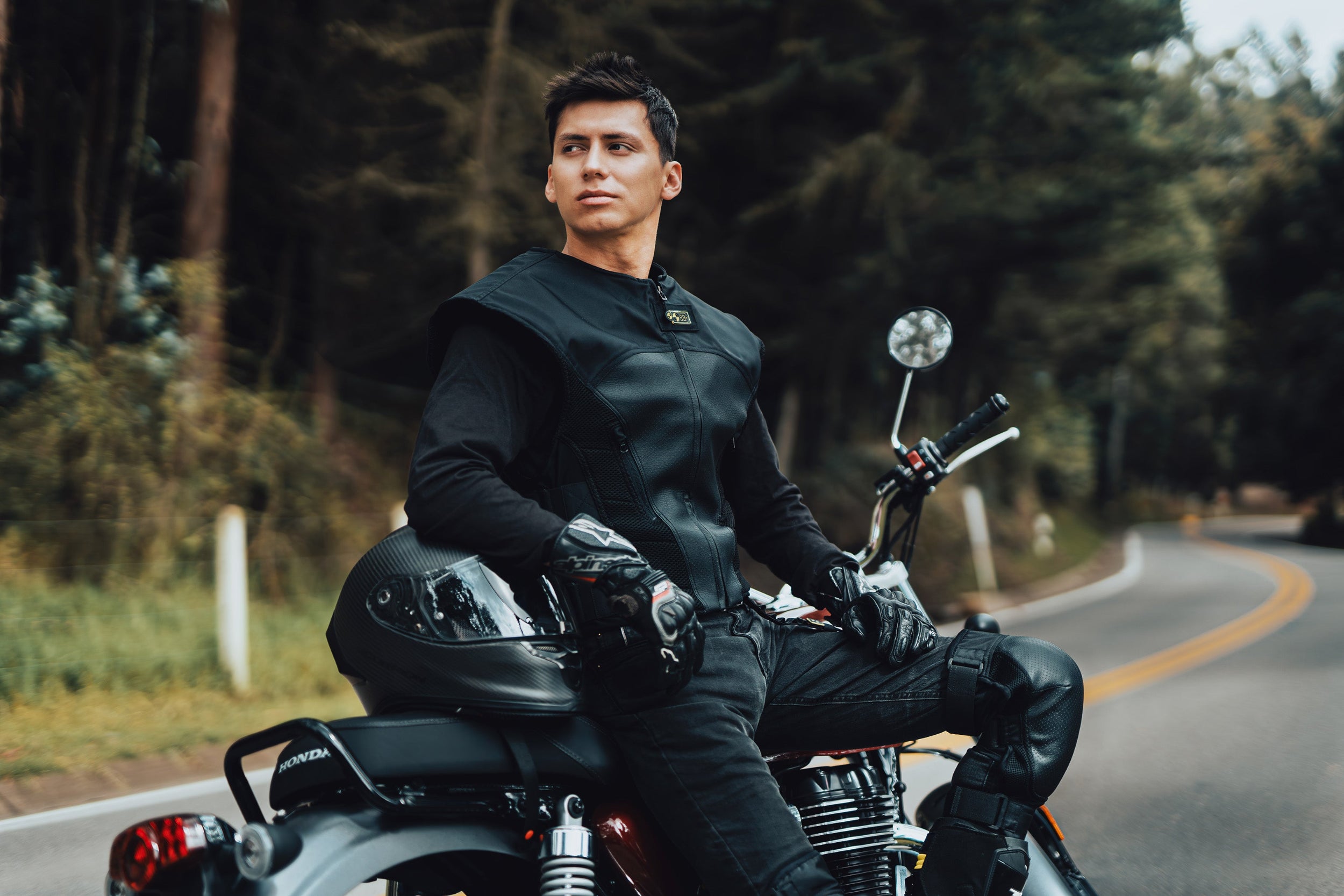 Motorista posando sobre su motocicleta clásica en una carretera arbolada vistiendo el elegante chaleco airbag CHOPPER VEST.