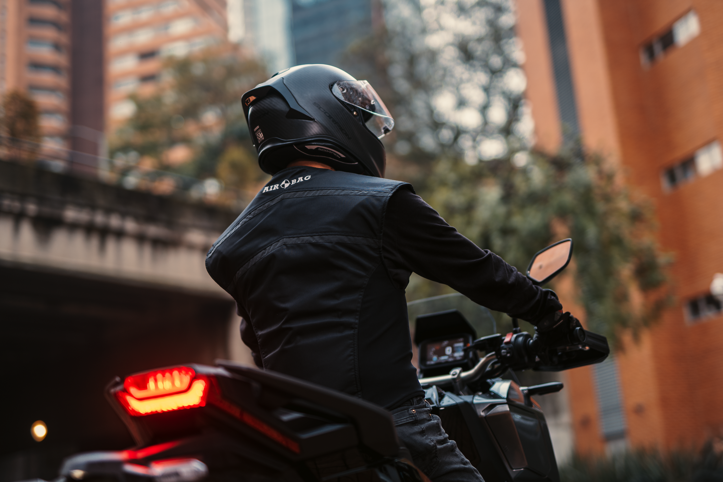 Vista trasera de un motorista en la ciudad vistiendo el chaleco airbag mecánico WISE VEST negro de Airobag, preparado para la ruta
