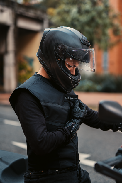 Primer plano de un motorista con casco ajustándose el chaleco airbag negro resistente WISE VEST de Airobag antes de iniciar su trayecto.